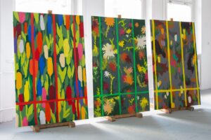 Zdjęcie przedstawia wizualizację stojących przy ścianie trzech obrazów autorstwa Bożeny Paluch pod tytułem „Ogród sąsiadki”. Są to wszystkie obrazy z tej serii. Obrazy z serii 