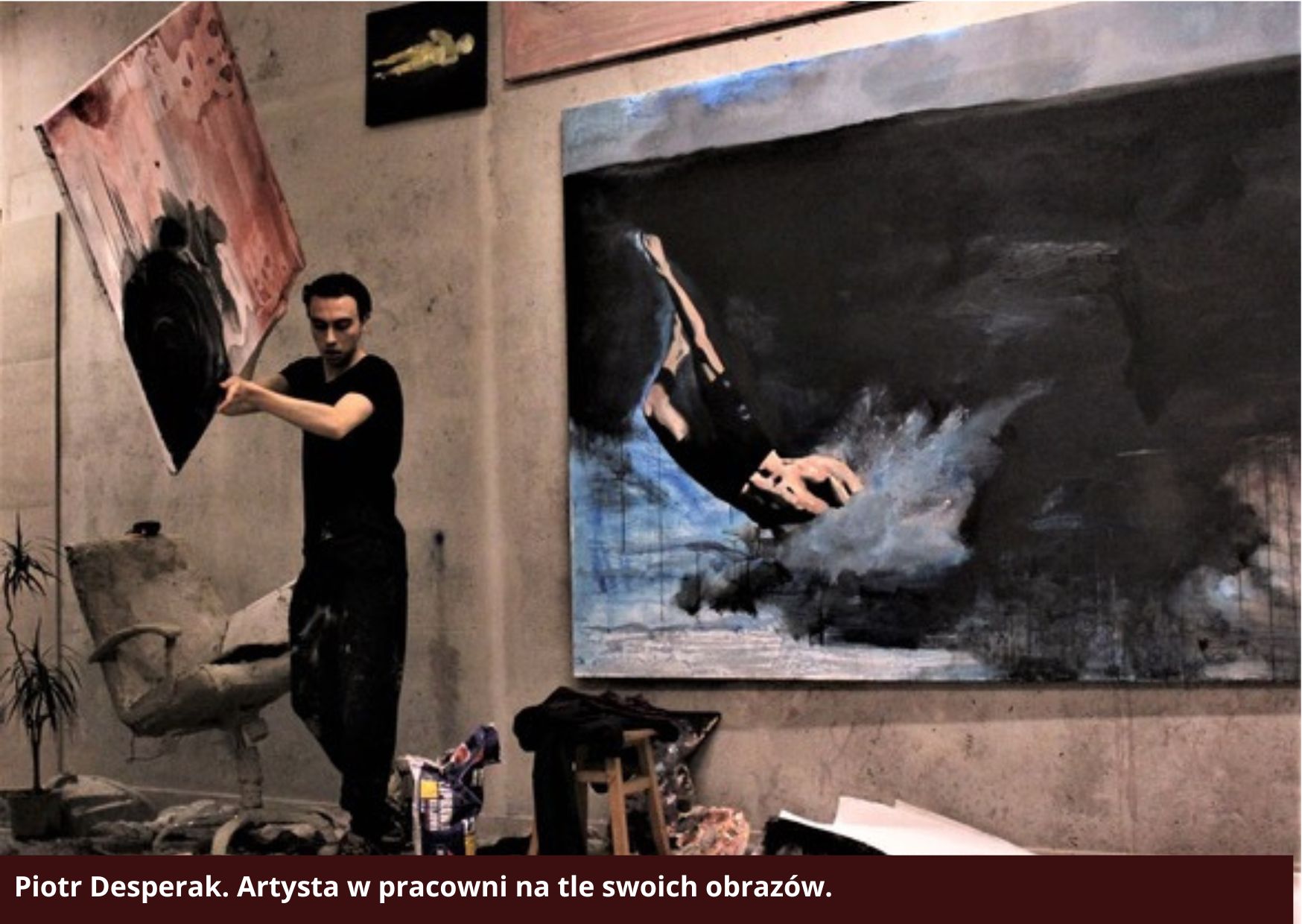 Zdjęcie przedstawia malarza Piotra Desperaka w pracowni, na tle swoich obrazów. Zdjęcie jest wykorzystane do profilu artysty na stronie Galerii Wiele Sztuki. 