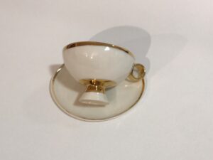 Piękna filiżanka do herbaty z białej porcelany, inspirowana powieścią „Alicja w krainie czarów”, z talerzykiem. Filiżanka jest wykonana z białej porcelany i jest ozdobiona 24-karatowym złotem: złoty pasek u styku czarki z nóżką, wokół rantu filiżanki i krawędzi talerzyka. To wzór klasycznej elegancji. Produkt dostępny w Galerii Wiele Sztuki.