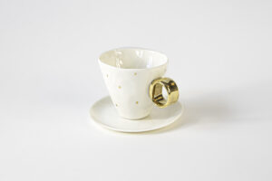 Piękna, kunsztowna filiżanka z talerzykiem, do pojedynczego lub podwójnego espresso z serii Piegowata księżniczka. Filiżanka jest ozdobiona na korpusie małymi kropkami ze złota i ma w całości pozłacane uszko. Jest wykonana z białej porcelany AUDREY BLACKMAN znanej z gładkości, pięknej bieli i przejrzystości. Produkt dostępny w Galerii Wiele Sztuki.