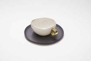 Piękna, filigranowa filiżanka do herbaty z białej porcelany z delikatnie złoconym rantem i złoconym uszkiem. W komplecie z filiżanką jest talerzyk z czarnej matowej porcelany z subtelnymi złotymi zdobieniami w formie małych kropli. Złocenia wykonane z 24-karatowego złota. Produkt dostępny w Galerii Wiele Sztuki.