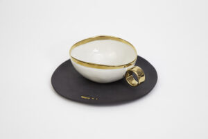 Piękna, filigranowa filiżanka do herbaty z białej porcelany ze złoceniami. W komplecie z filiżanką jest talerzyk z czarnej matowej porcelany z subtelnymi złotymi zdobieniami w formie małych kropek. Produkt dostępny w Galerii Wiele Sztuki.