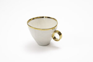 Piękny kubek z białej porcelany, z wyraźnym złoceniem na brzegu i złotym uszkiem. Produkt dostępny w Galerii Wiele Sztuki.
