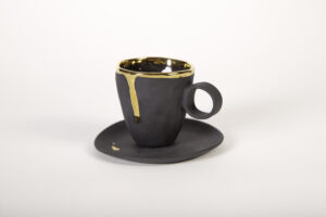 Piękna, kunsztowna filiżanka z porcelany w kolorze czarnym z talerzykiem, do pojedynczego lub podwójnego espresso z serii Mały Książę. Zdobienie tej czarnej porcelany to 24-karatowe złoto, które otoczyło cały rant, a spadając delikatną kroplą na pozostawiło ślad na boku filiżanki. Produkt dostępny w Galerii Wiele Sztuki.