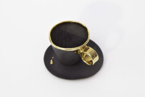 Piękna, kunsztowna filiżanka z porcelany w kolorze czarnym z talerzykiem, do pojedynczego lub podwójnego espresso z serii Książę. Filiżanka ma pełne elegancji i stylu zdobienie z 24-karatowegwo złota: złote ucho, złoty rant i delikatna kropla złota na talerzyku. Produkt dostępny w Galerii Wiele Sztuki.