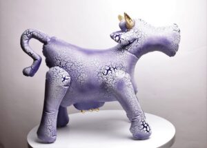 Wielkoformatowa rzeźba ceramiczna 'Krówka Woodoo' Mariusza Dydo, fioletowo-lawendowa figura krowy z unikatową siecią drobnych spękań szkliwa i złotymi rogami, Galeria Wiele Sztuki.